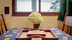 Een eettafel met een tafelkleed met bloemenprint, een vaas met witte bloemen en een houten dienblad met een boek.
