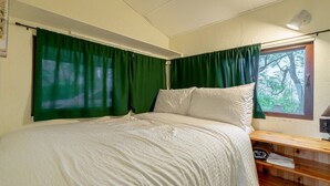 Een slaapkamer met een bed, groene gordijnen, een raam met uitzicht op bomen en een houten plank met een handdoek.