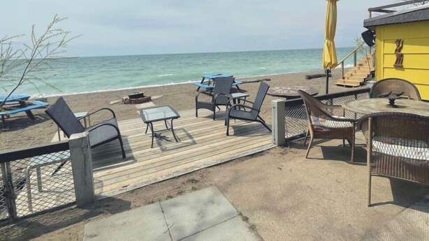 Een terras aan het strand met buitenmeubilair en een geel gebouw.