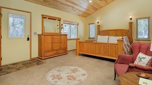 Ein Schlafzimmer mit Holzboden, einem großen Bett, einem roten Sessel und einer Holzkommode.