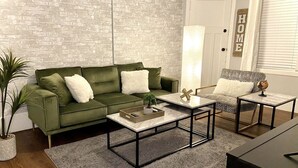 A living room with a green sofa, a coffee table, a side table, and a potted plant. - NEW! Cozy Stay in Newly Decorated Apt, in Midtown! (Detroit)