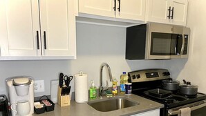 A kitchen with white cabinets, a stainless steel microwave, a stove, and a coffee maker. - NEW! Cozy Stay in Newly Decorated Apt, in Midtown! (Detroit)