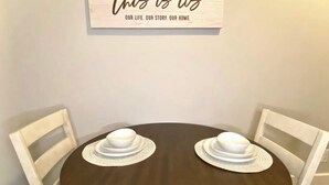 A round wooden table with two white chairs, each with a hat on top. A framed sign above reads "Our Life. Our Story. Our Home." - NEW! Cozy Stay in Newly Decorated Apt, in Midtown! (Detroit)