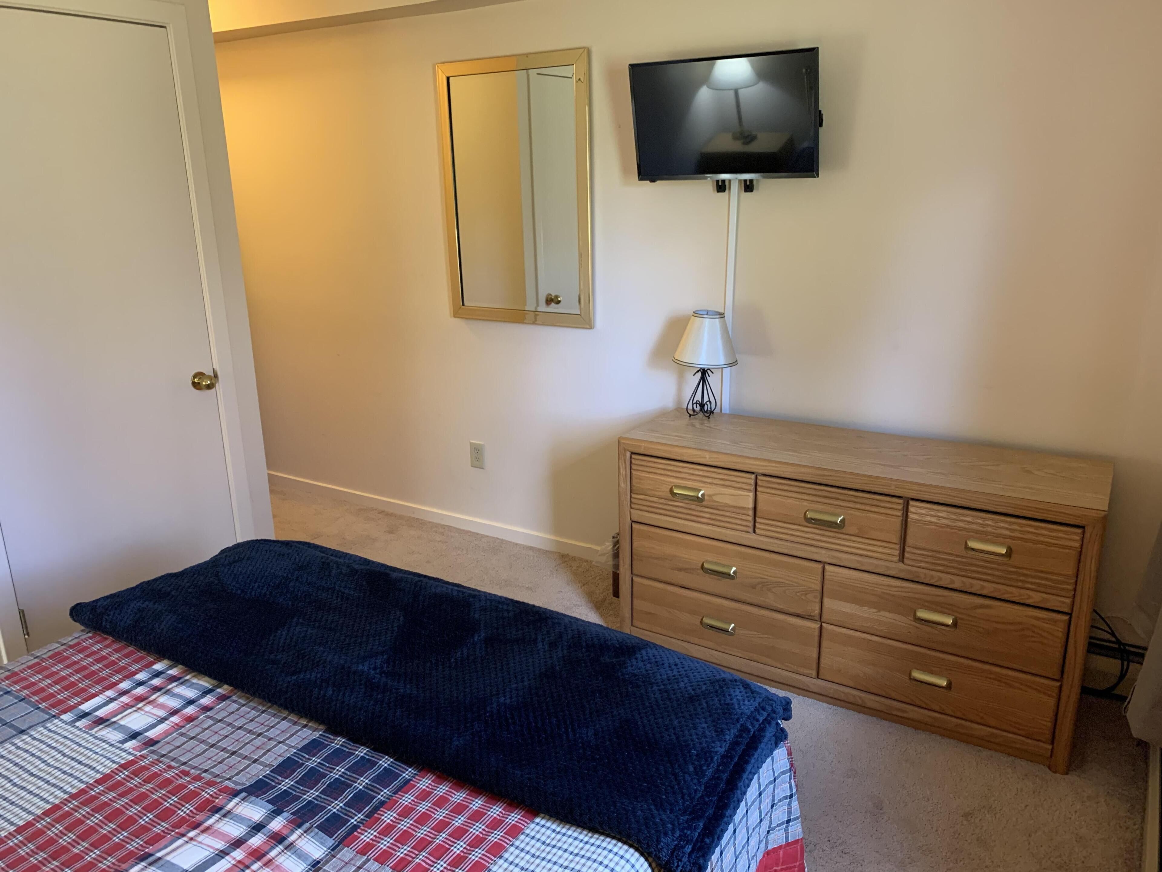 Une chambre à coucher avec un lit, une commode, un téléviseur fixé au mur et un miroir.