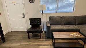 Ein Wohnzimmer mit dunklem Holzboden, einem schwarzen Ledersessel, einem grauen Sofa und einem Couchtisch mit einer Zeitschrift darauf.