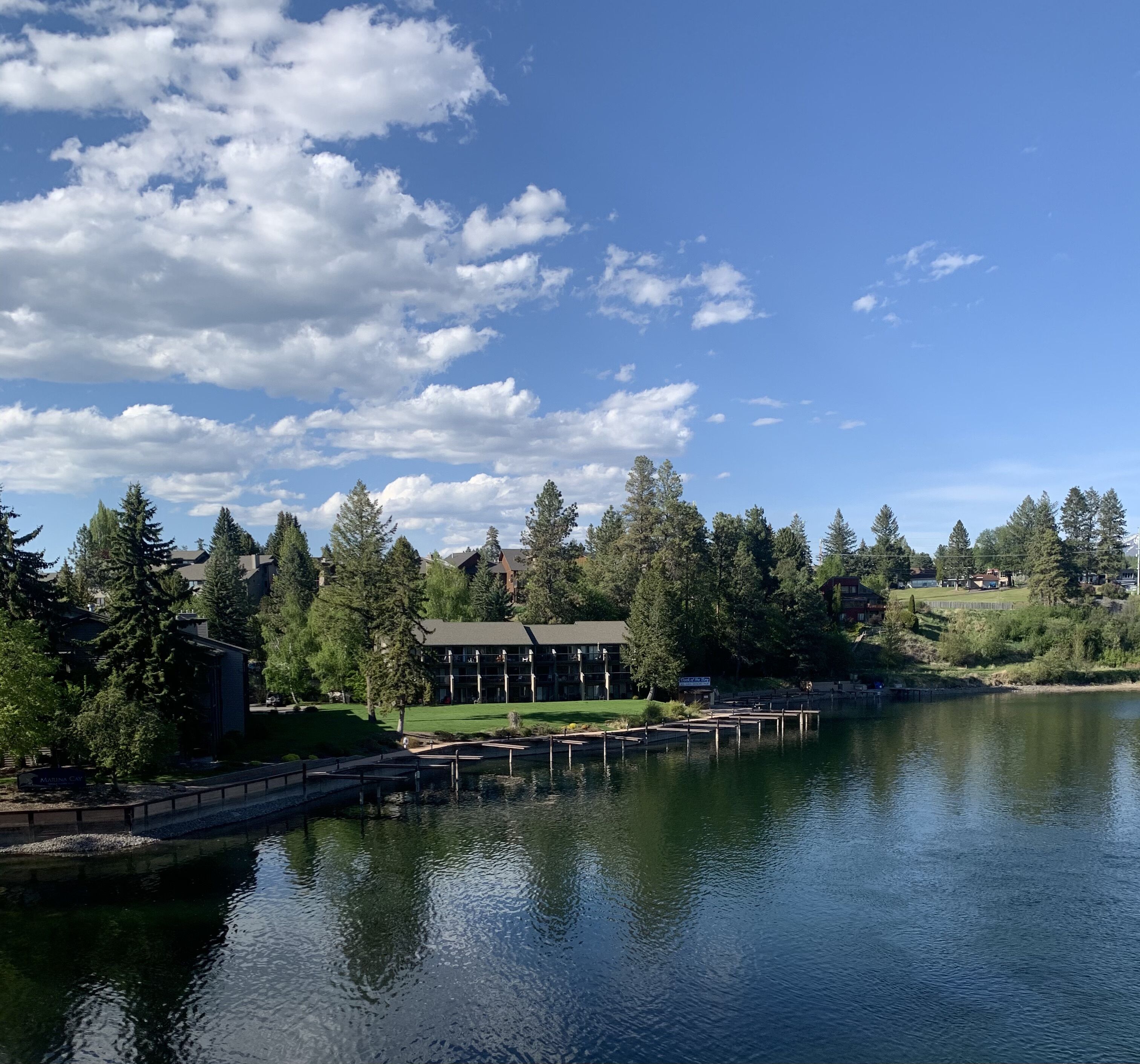 A lakeside view with a building surrounded by trees, a dock, and a clear sky.