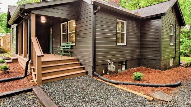 A two-story house with a front porch, a chimney, and a small garden area with mulch and gravel. - Deacon Stays: The Brookwood - Walk to WFU (Winston-Salem)