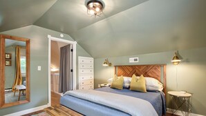 A bedroom with a large bed, a wooden headboard, a bench, a mirror, and a small table with a lamp. - Deacon Stays: The Brookwood - Walk to WFU (Winston-Salem)