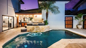 Une maison moderne dotée d’une piscine, d’une cuisine avec un coin bar et d’un patio agrémenté d’un palmier.
