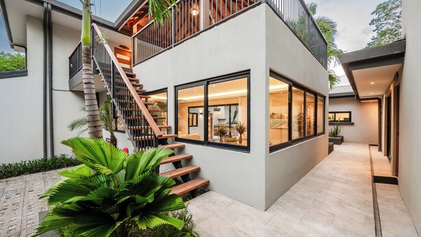 Une maison moderne à deux étages, dotée d’un escalier, de grandes fenêtres et d’un balcon.