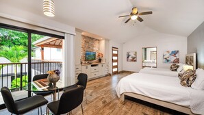Een moderne slaapkamer met een groot bed, een zithoek met een glazen tafel en een keuken met een stenen wand.