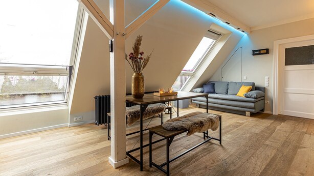 Ein modernes Schlafzimmer im Loft-Stil mit schrägem Dach, Dachfenster und einer gemütlichen Sitzecke mit Sofa und Bank.