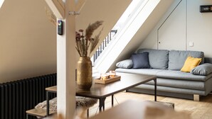 Ein modernes Schlafzimmer im Loft-Stil mit schrägem Dach, einer grauen Couch mit Kissen, einem kleinen Holztisch mit einer Vase und einem Heizkörper.