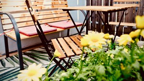 Eine Holzbank mit rotem Kissen, ein Holztisch und gelbe Blumen im Vordergrund.
