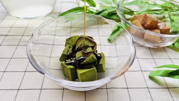 Un tazón de vidrio transparente con cubitos de hielo de matcha y un hilo de jarabe, sobre un mantel a cuadros.