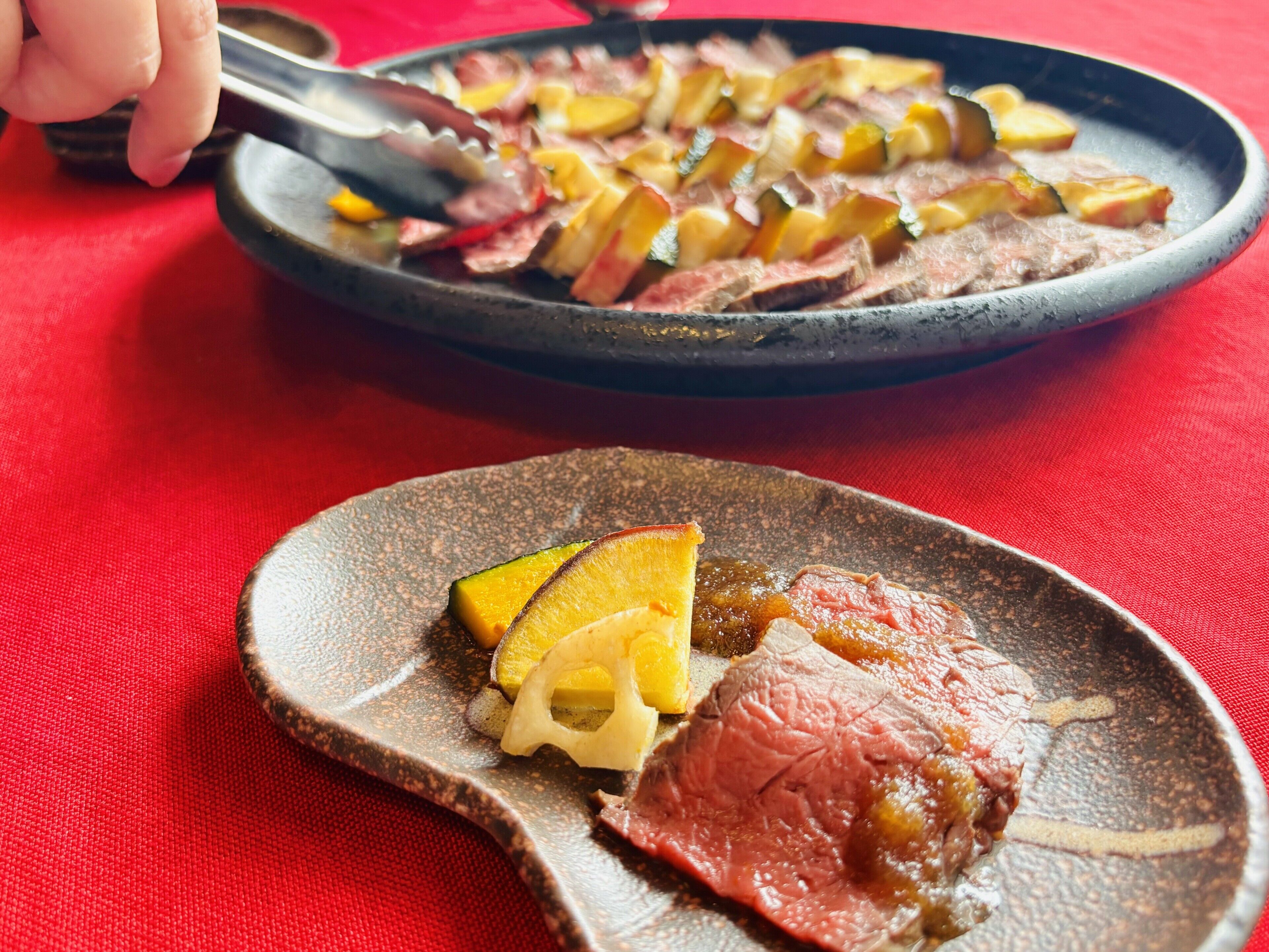 A plate of food with meat and vegetables on a red tablecloth.