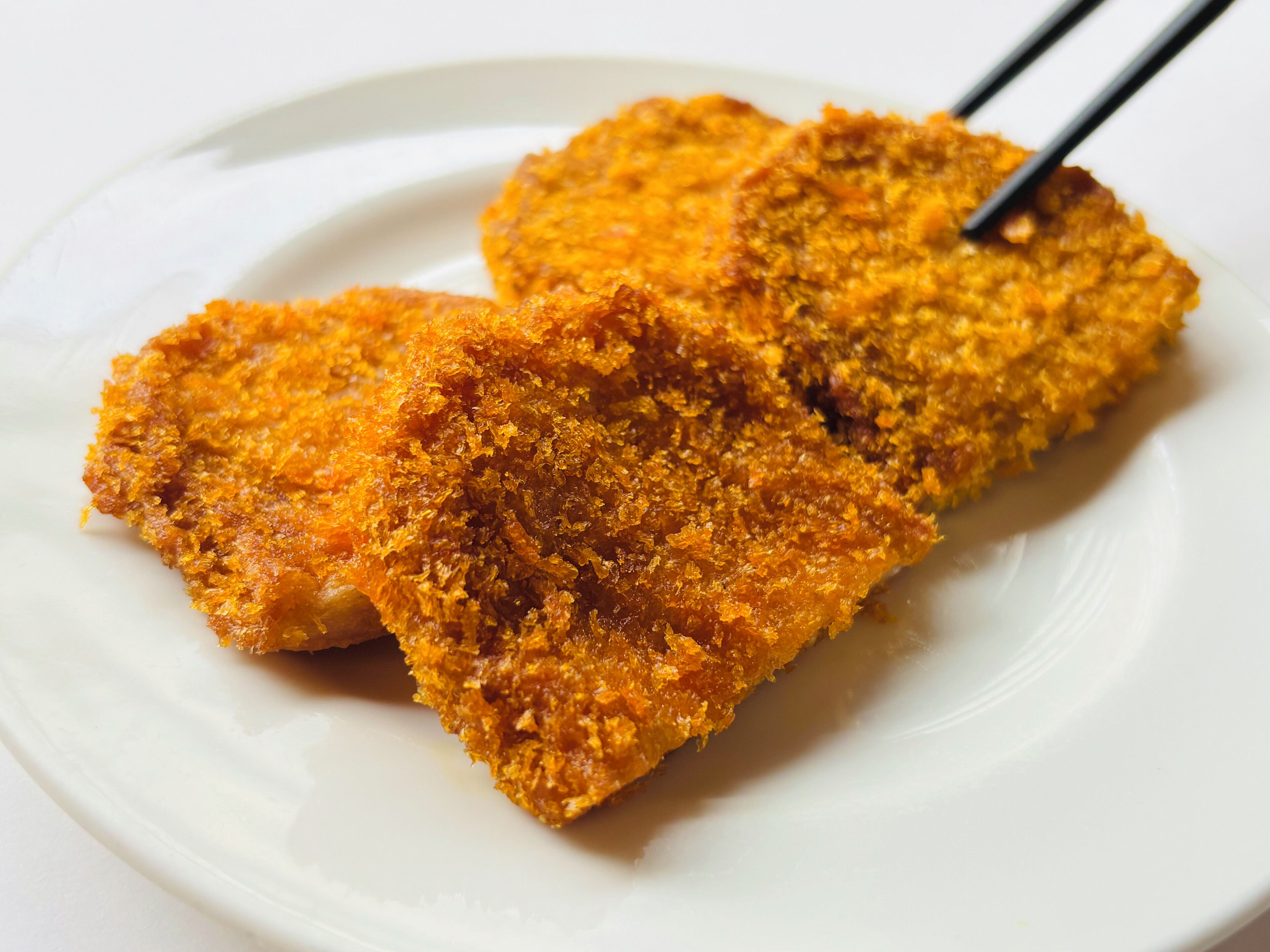 Two breaded and fried items on a white plate with chopsticks.