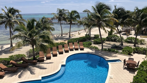 Ein Poolbereich mit Liegestühlen und Palmen, mit Blick auf einen Strand und das Meer.