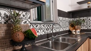 A kitchen with a stainless steel sink, a woven basket with a pineapple and a watermelon, and a decorative vase on the counter.