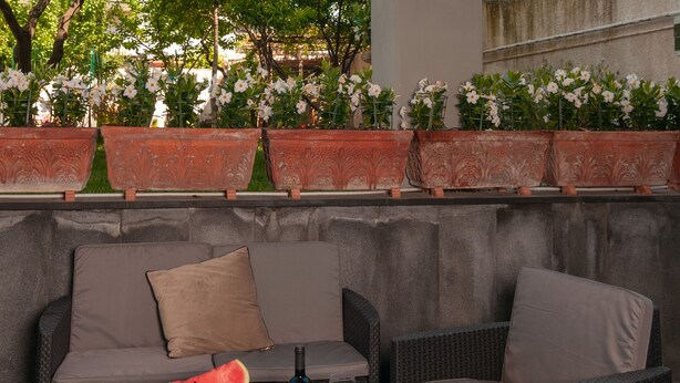 An outdoor seating area with wicker furniture, a table with a bottle, glasses, and strawberries.