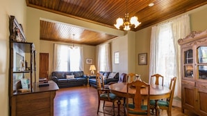 A spacious living room with a wooden ceiling, a dining area with a wooden table and chairs, and a built-in cabinet with glass doors.