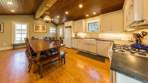 A spacious kitchen with wooden floors, white cabinets, a dining table, and a gas stove.