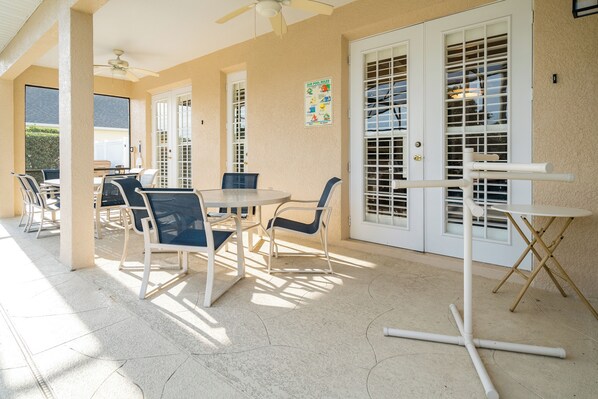 Un área de patio techada con una mesa redonda y sillas, un ventilador de techo y una mesa plegable.