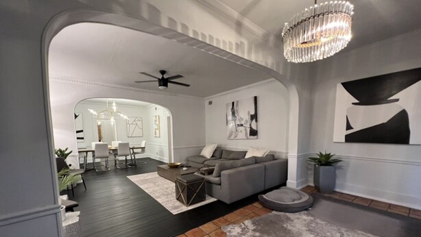 Un salon moderne avec un canapé gris, une table basse et un tapis. On aperçoit à l’arrière-plan un coin repas avec une table et des chaises.