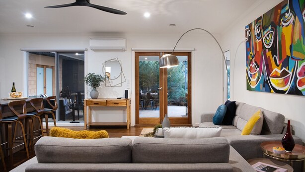 Una sala de estar moderna con un sofá gris, un comedor con sillas de madera, un ventanal grande y un cuadro abstracto colorido en la pared.