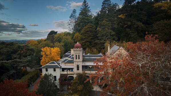 Un bâtiment historique doté d’une tour imposante, entouré d’une forêt dense et des couleurs automnales des arbres.