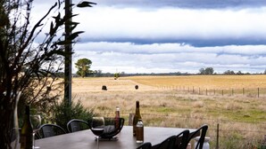 Una mesa con copas y botellas de vino, con vistas a un campo con vacas y una valla.