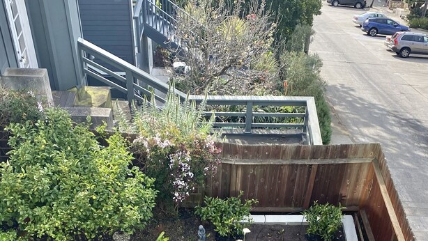 Un patio al aire libre con un sofá azul, una mesa de madera y sillas. Hay plantas en macetas y una terraza de madera.