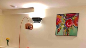 Una sala de estar moderna con un sofá blanco, cojines coloridos, una mesa de centro de cristal, una lámpara de pie y un cuadro llamativo en la pared.