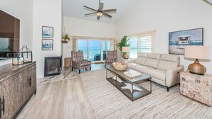 A spacious living room with a large window, a ceiling fan, and a view of the ocean.