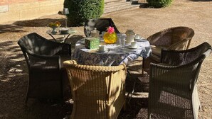 A courtyard with a table set for tea, wicker chairs, and a building with blue shutters and a balcony. - Villa Tourterelle (Caussade)