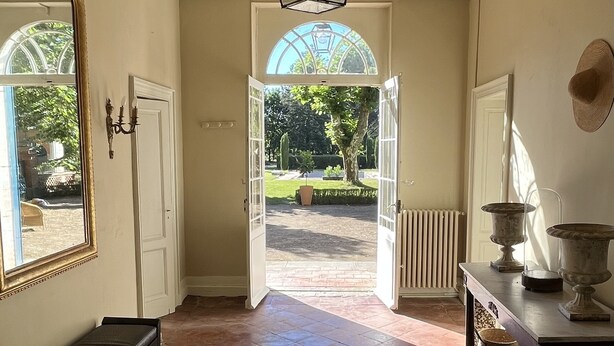 A spacious hallway with a large mirror, a round rug, and a view of a garden through open doors. - Villa Tourterelle (Caussade)