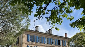 A large, historic building with multiple windows and a symmetrical facade, surrounded by a well-maintained lawn and tall trees. - Villa Tourterelle (Caussade)