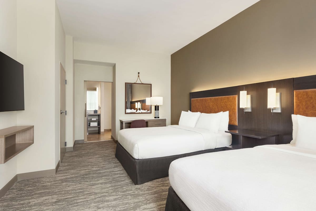 A hotel room with two beds, a desk with a chair, a flat-screen TV, and a mirror.
