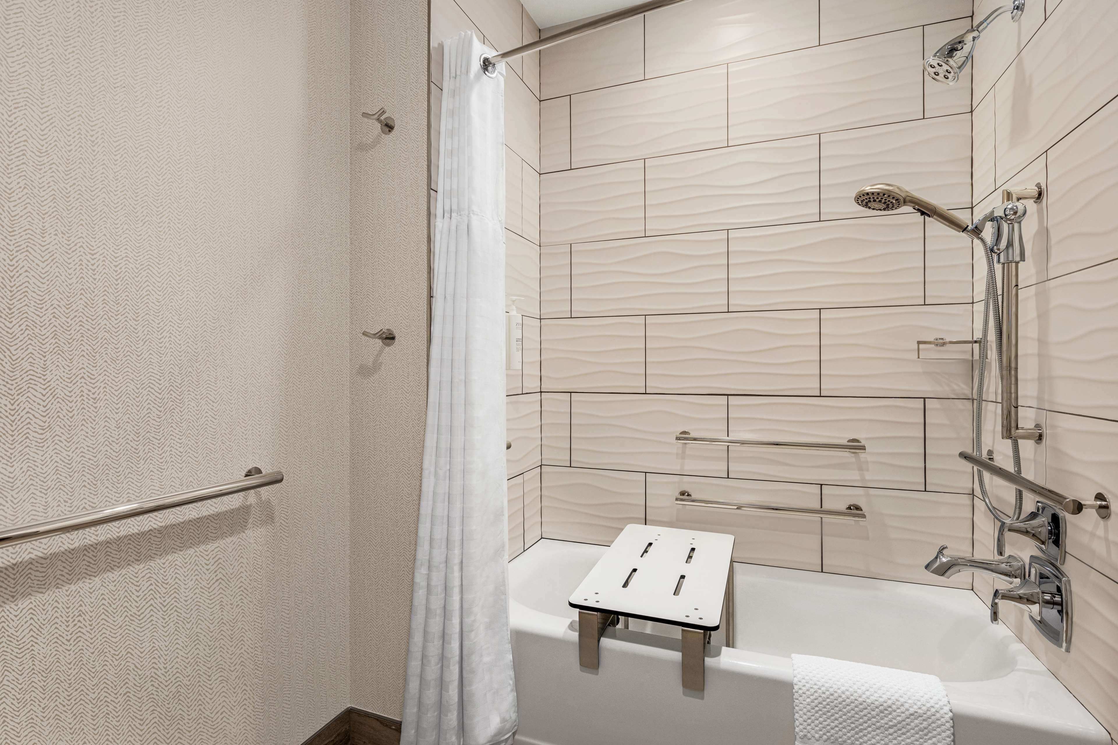 A modern bathroom with a shower, a bathtub with a small stool, and a towel rack.