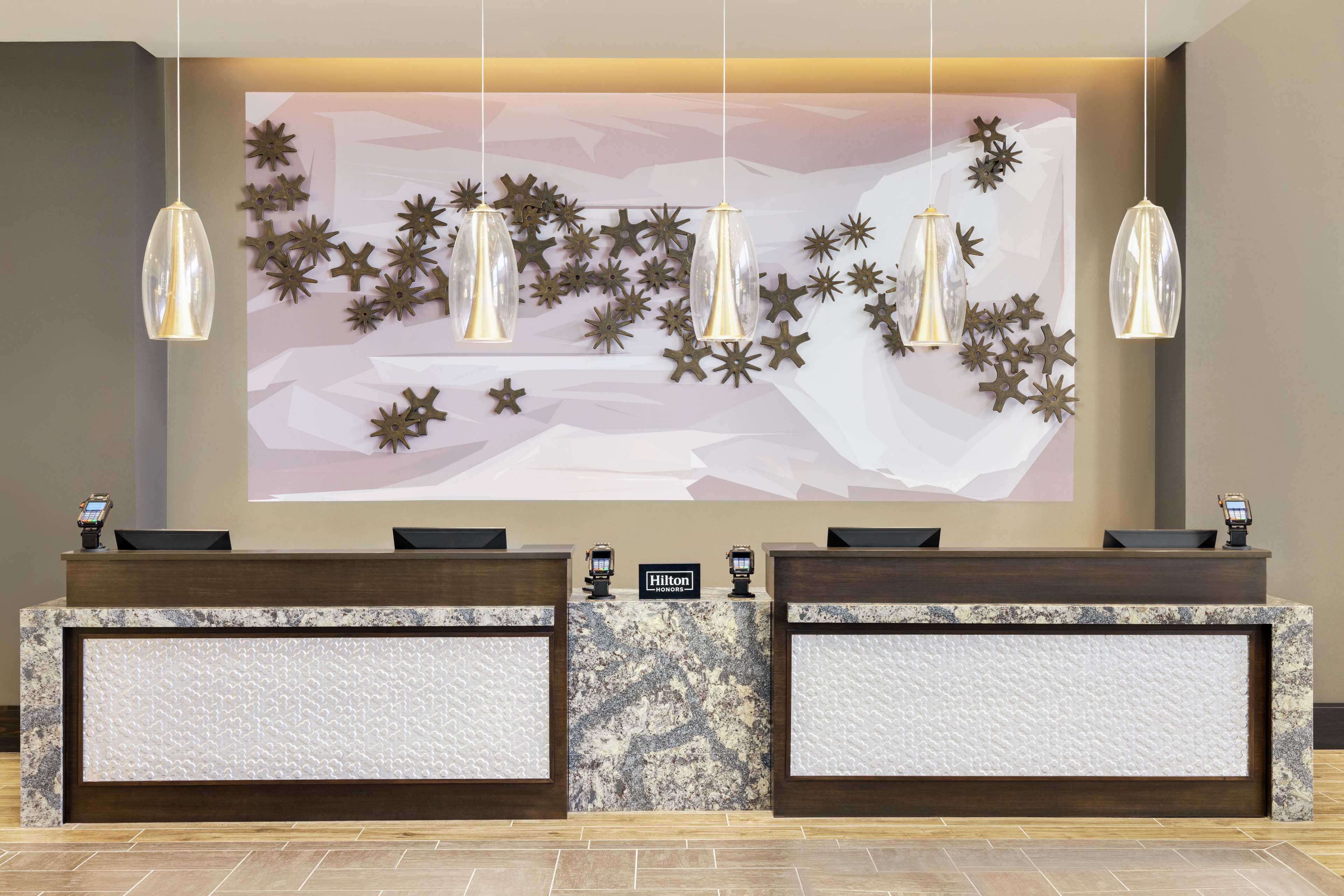 A hotel reception desk with a marble top, two black chairs, and a large wall mural with star decorations.