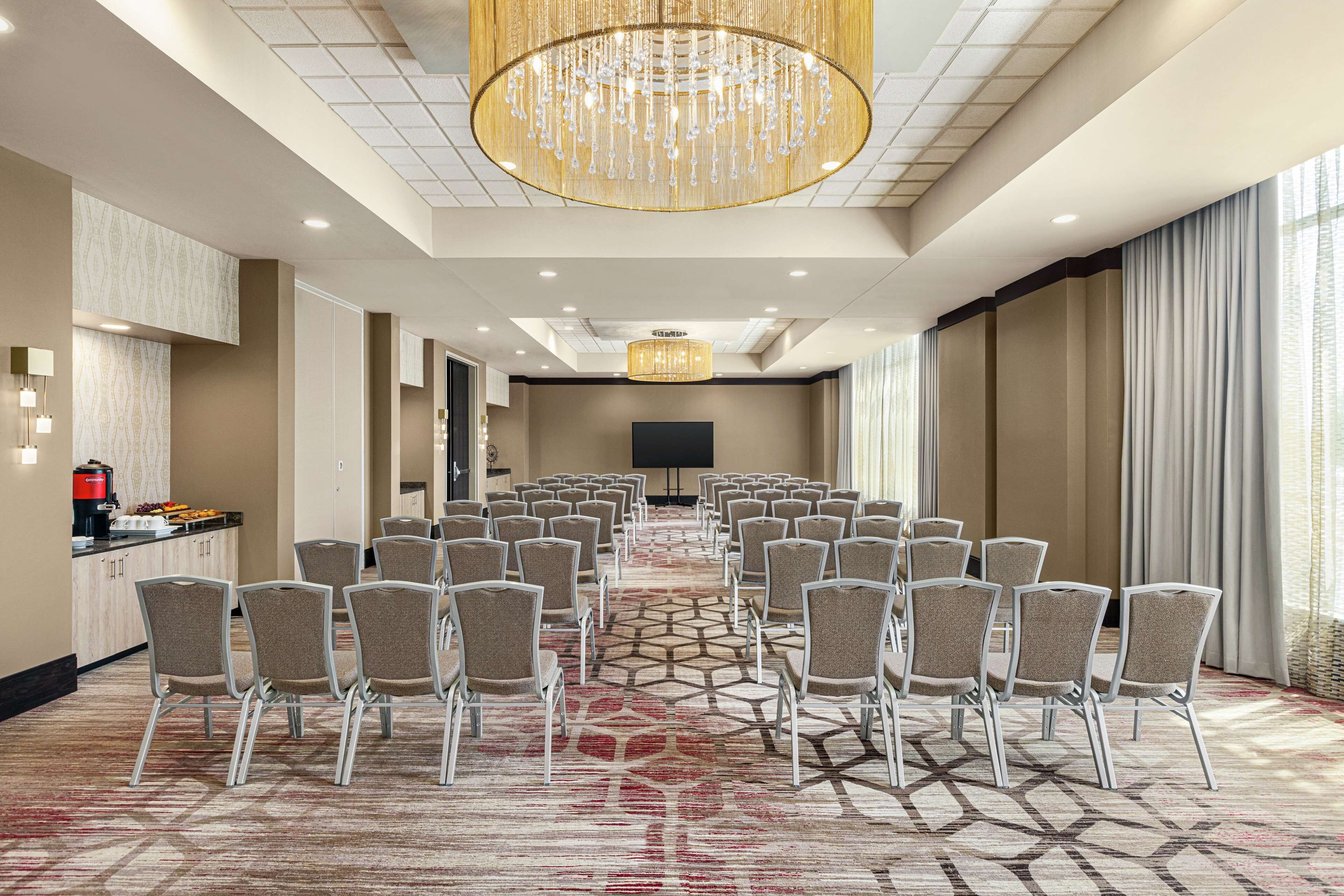 A conference room with rows of chairs, a large chandelier, a flat-screen TV, and a buffet area.