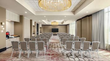 Une salle de conférence avec des rangées de chaises, un grand lustre, un téléviseur à écran plat et un espace buffet.