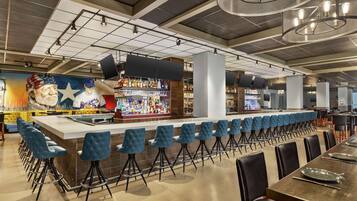 A modern bar area with a long counter, blue bar stools, and a mural of a historical figure.