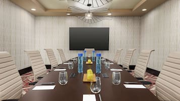 Une salle de conférence équipée d’une longue table, de chaises, d’un écran de projection et d’un lustre moderne.