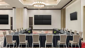 A conference room with a long table, chairs, a chandelier, and a flat-screen TV on the wall.