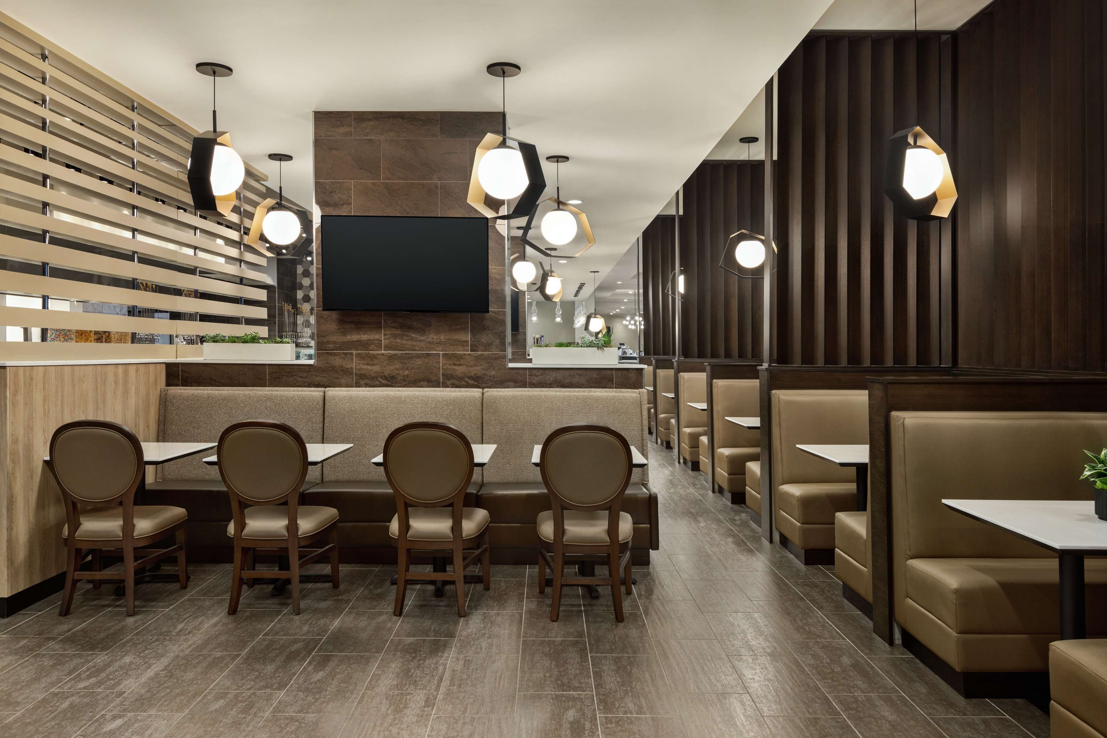 A modern restaurant interior with wooden slats, cushioned booths, and pendant lighting.