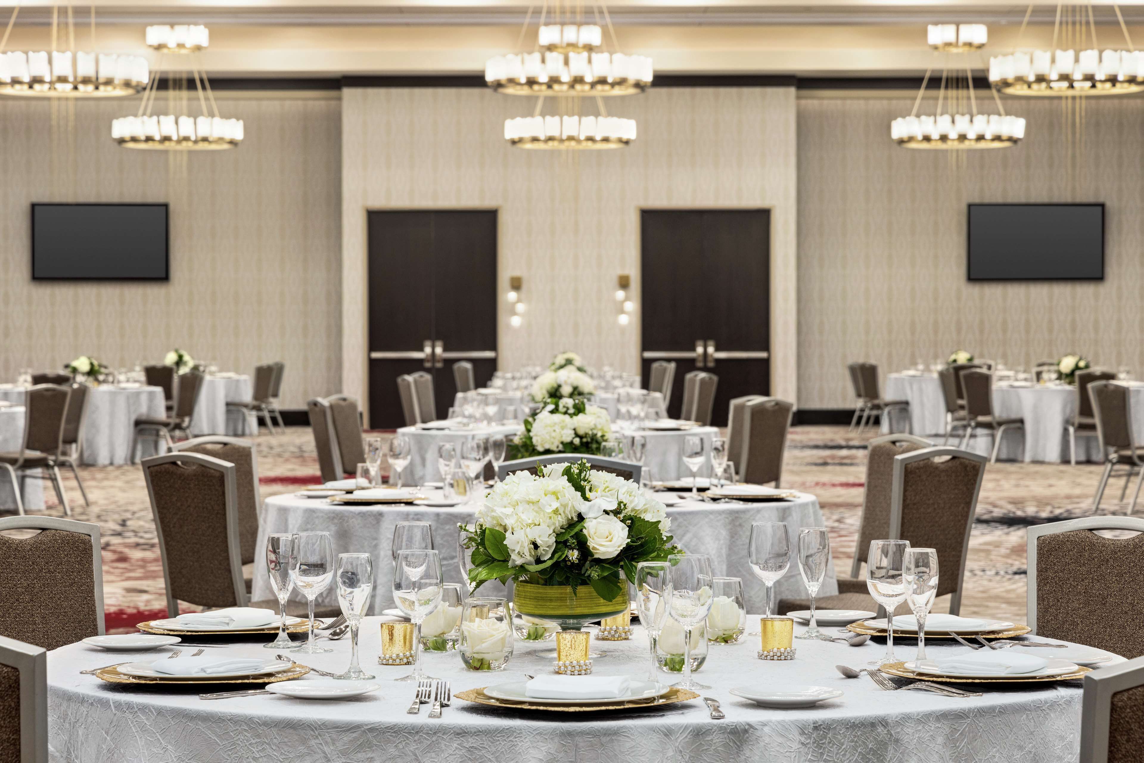 A banquet hall with round tables set for dining, each with white tablecloths, gold chargers, and clear glassware.