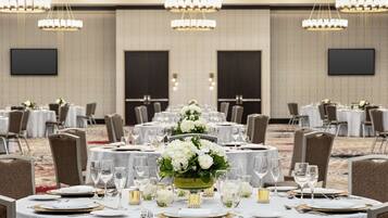 A banquet hall with round tables set for dining, each with white tablecloths, gold chargers, and clear glassware.