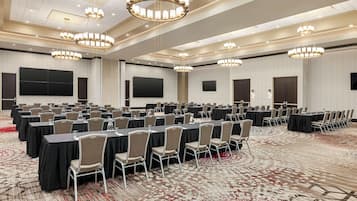 Une grande salle de conférence avec de nombreuses tables et chaises disposées en rangées, plusieurs écrans et des lustres.
