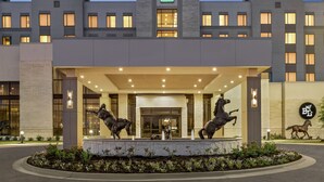 A modern hotel entrance with a central fountain, a prominent 'E' logo, and a landscaped area with flowers. - Embassy Suites by Hilton Round Rock (Round Rock)